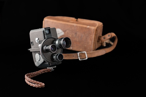 A vintage camera displayed on a black background beside a brown carry case