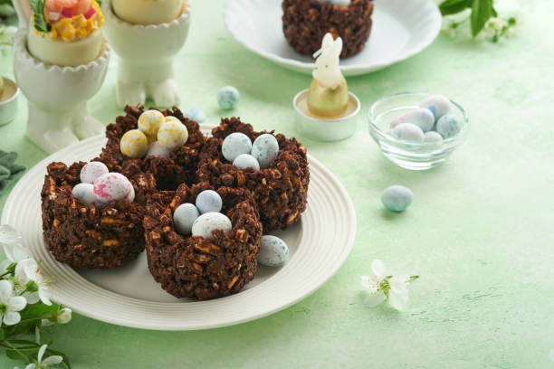 istock Easter chocolate nest cake with mini chocolate candy eggs with blossoming cherry or apple flowers on green background table. Creative recipe for Easter table with holiday decorations. Top view. 1700292872