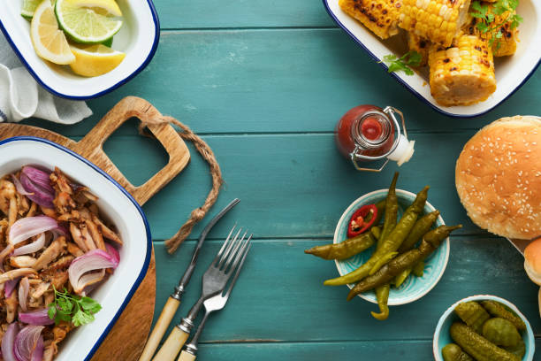 istock Pulled bbq chicken with baked onions on serving platter, bbq corn, pickles, chili peppers and buns for hot dogs and burgers, tomato sauce. Traditional American grilled summer bbq sandwiches dishes. 1700293992