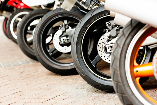 A row of varied motorcycle wheels lined up on the diagonal on a brick-paved surface