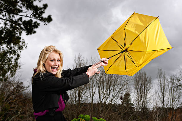 A gust of wind blows a startled, laughing woman's umbrella inside-out, leaving her at the mercy of the rain.