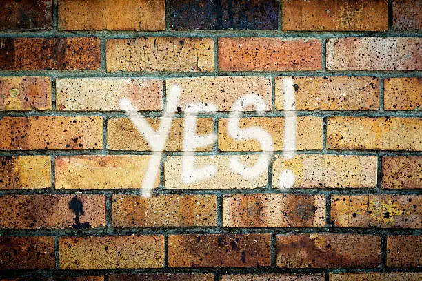 Graffiti on a  grungy brick wall says "YES!" Someone approves of something! 