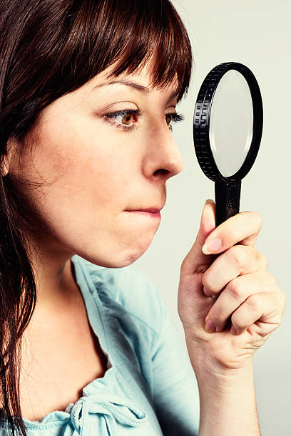 istock Frowning young woman peers through magnifying glass at something 170029928