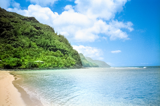 Vintage 1970s film photograph of Ke'e beach and the ocean through lush green hills on the tropical island of Kauai, Hawaii.