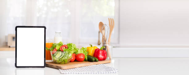 istock Tablet computer, plate with fresh salad and different products in kitchen background with space for text. tablet with mockup white screen on vegetarian healthy food vegetable background. 1700314108