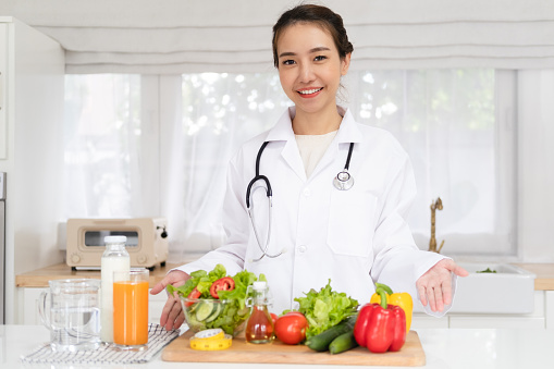 smiling Asian nutritionist looking at camera and showing healthy vegetables and fruit in the consultation. Weight loss and right nutrition concept