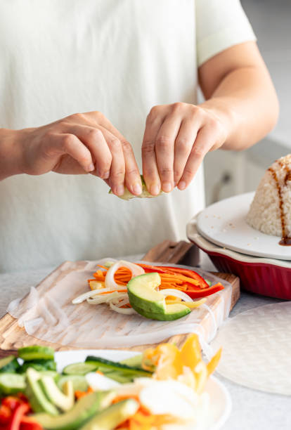 istock Woman preparing spring rolls in rice paper on kitchen table. 1700326202