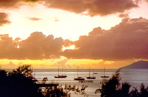 Vintage 1970s film photograph of a vibrant Hawaiian volcanic orange sunset over the ocean horizon with silhouette of sailboats.