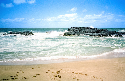 Vintage 1970s film photograph of the lava fields of black volcano rock against the blue waters and sandy beach on the tropical island of Maui, Hawaii.