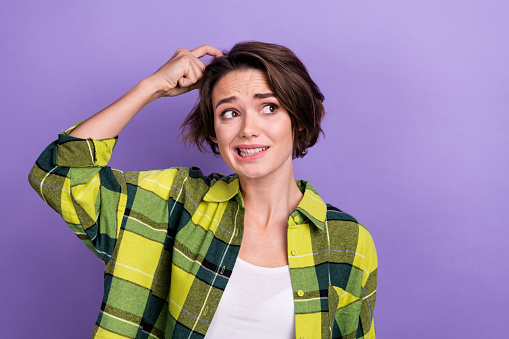 Portrait of hesitant young woman nervous scratch head looking empty space do not remember password isolated on violet color background.