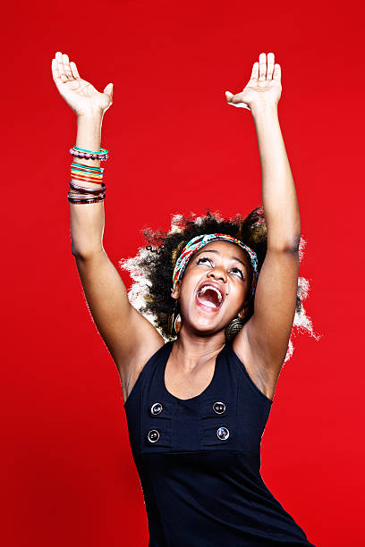 Gospel singing or praise dancing, young afro-haired woman is ecstatic A cute young woman with Afro-style hair looks up in ecstasy, possibly a gospel singer or praise dancer but definitely full of joy. against a red background. black female gospel singers stock pictures, royalty-free photos & images
