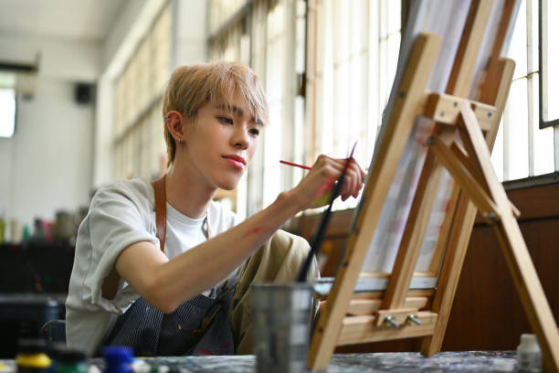 Portrait image of LGBT artist, an Asian male teenager with colored hair doing artwork in the workshop studio Portrait image of LGBT artist, an Asian male teenager with colored hair doing artwork in the workshop studio. trans boy stock pictures, royalty-free photos & images