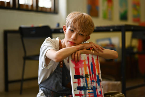 Young Asian LGBT artist boy with colored hair proudly embracing his artwork. Young Asian LGBT artist boy with colored hair proudly embracing his artwork.. trans boy stock pictures, royalty-free photos & images