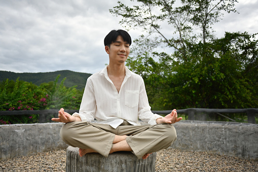 Young Asian woman is practicing yoga and meditating in green nature in Slovenia. She is focused on practice and is enjoying the sun.
