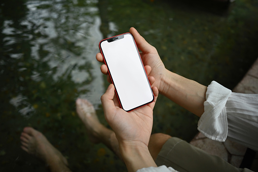 A male's hand holding a smartphone with the empty screen while soaking his feet in the hot springs.