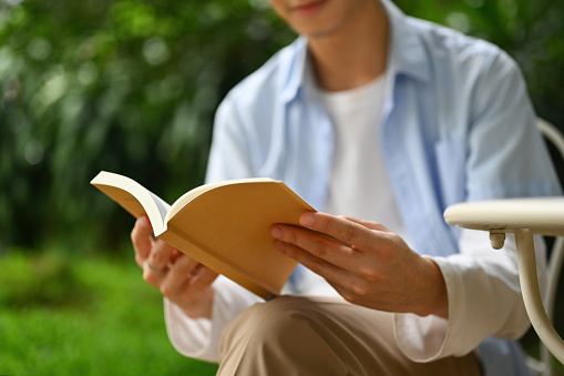 Close up image of A young Asian man reading a book in the garden, selective focus on hand.