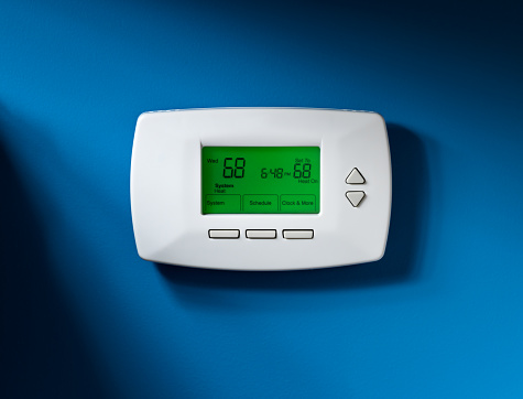 Programmable thermostat set to 68 degrees.  Isolated on blue background with dramatic lighting.