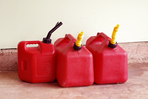 Three plastic gas containers are sitting on a concrete garage floor. Concept of hoarding or stockpiling gas to combat rising prices or possible shortages.
