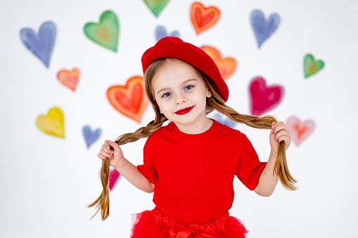 portrait of a little girl in a red beret and clothes on a background of colorful hearts, a smiling child, the concept of valentine's day and love