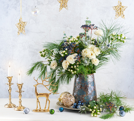 Christmas decorations, candles and flower bouquet. Winter arrangement with roses, fir branches, winter berries. Christmas flower still life.