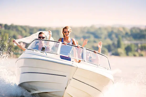 Group of young people with raised hands enjoying in a speedboat ride.   