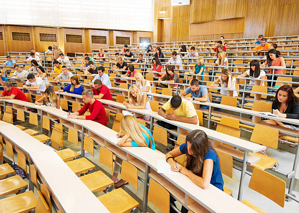 Large group of students doing exam. Group of college students at the university amphitheatre, they are sitting and doing an exam.   amphitheater stock pictures, royalty-free photos & images