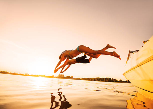 deux personnes sautant dans l'eau avec la lumière du soleil. - motorboat nautical vessel speedboat lake photos et images de collection