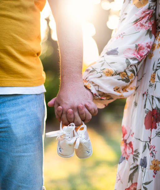 Holding hands, husband and wife hold their newborn baby's shoes a husband and wife holding baby shoes. Expectant parents expecting a baby announce stock pictures, royalty-free photos & images