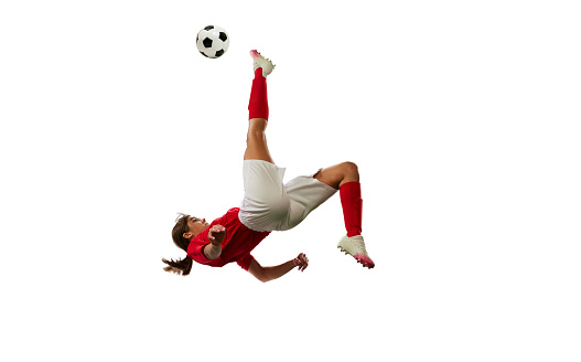 Competitive young girl, football player in motion, kicking ball and falling down isolated over white background. Concept of professional sport, competition, game, training, youth, action, ad