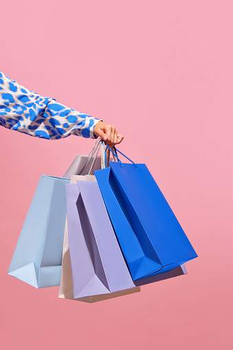 Sale offer. Black Friday. Shopping discount. Closeup of lady's hand holding purchase blue bags isolated on pink empty space background. concept of shopping, cyber monday. copy space for ad