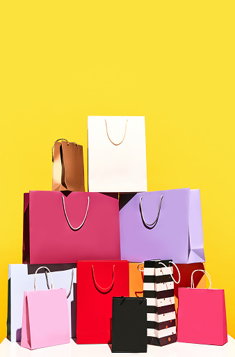Sale offer. Black Friday. Shopping delivery. Vertical photo of purchase colorful paper bags isolated on yellow background. concept of fashion, beauty, shop, salesperson, brand, trends. copy space. ad