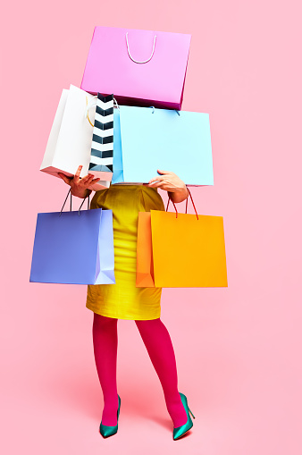 Unrecognizable woman in stylishly outfit carrying a lot of purchases, shopping paper bags over pink studio background. concept of fashion, beauty, salesperson, Black Friday, sale. copy space. ad