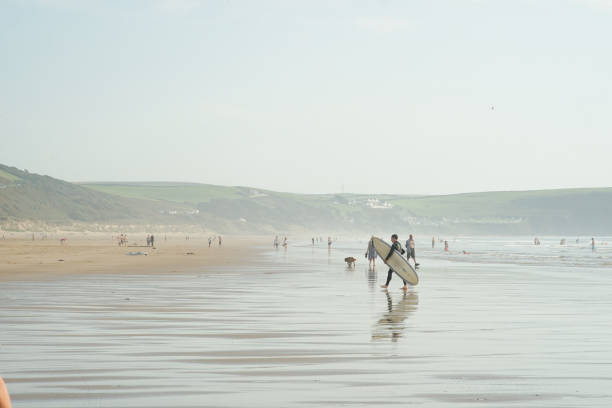 Woolacombe, England, UK - September 02, 2023: A man walks on the Woolacombe beach with his surfboard.
