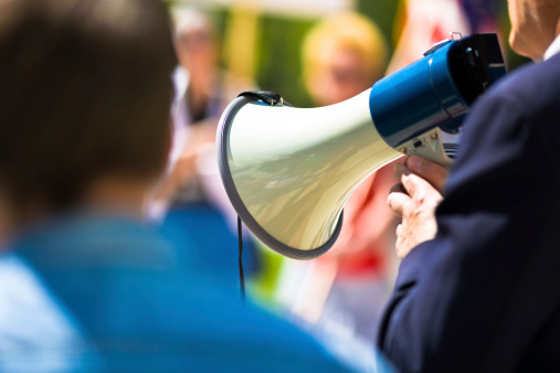Man holding a megaphone while speaking to a crowd. Very shallow DOF.