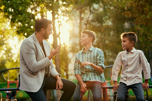 Man, attentive father spending time with his sons, talking, walking outdoors on warm sunny day. Love and care. Concept of family, childhood and parenthood, leisure time, fun