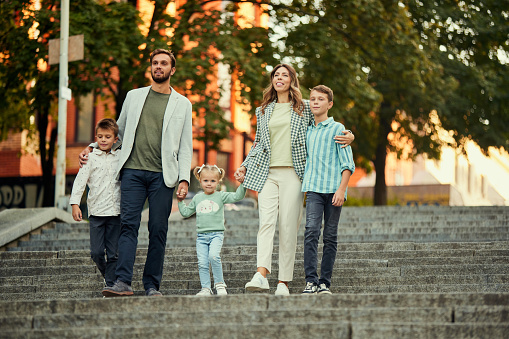 Beautiful young man and woman, mother and father walking in park down the stairs with their children, boys and girl on warm autumn day. Concept of family, childhood and parenthood, leisure time, fun