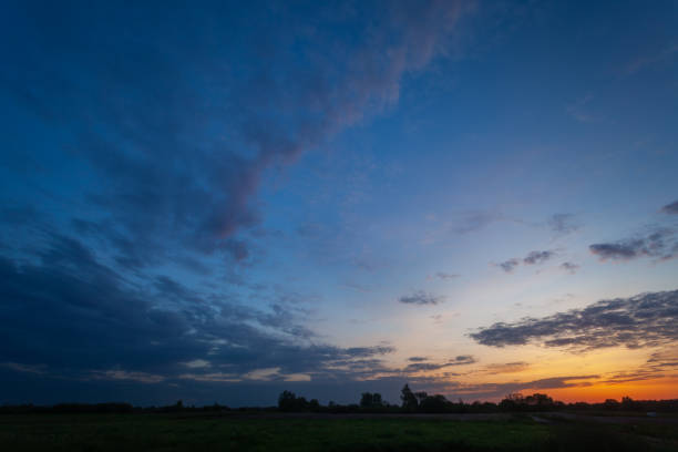 View of evening clouds and sky after sunset over a green meadow