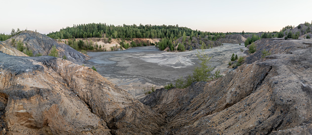 eroded soil quarry ravine with forest on its edge at summer evening panoramic photo.
