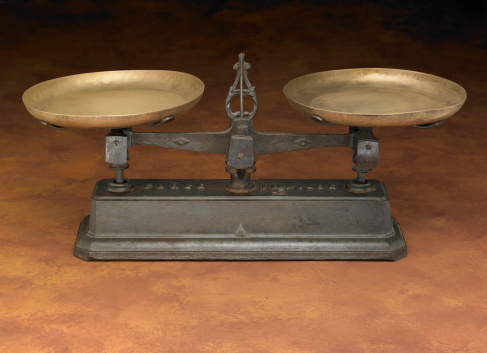An antique leveling scale on a warm-colored painted backdrop.
