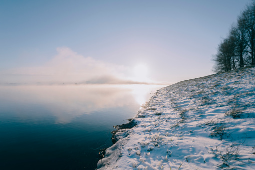 Mist rising up from the river IJssel during a cold winter morning  in the Netherlands. The water level is high and there is snow and ice on the levees on the shore of the river during this beautiful morning sunrise.