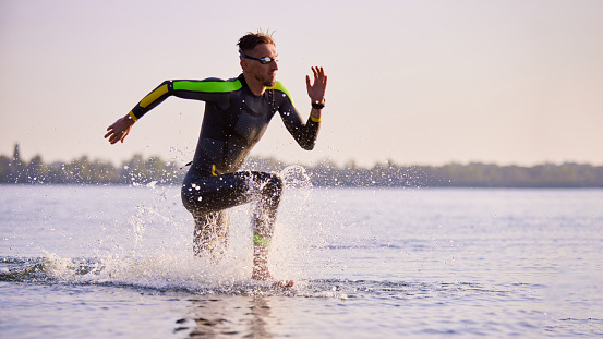 Mature man in wetsuit, sportsman, triathlon in wetsuit training outdoors, swimming into river. Concept of professional sport, triathlon preparation, competition, athleticism