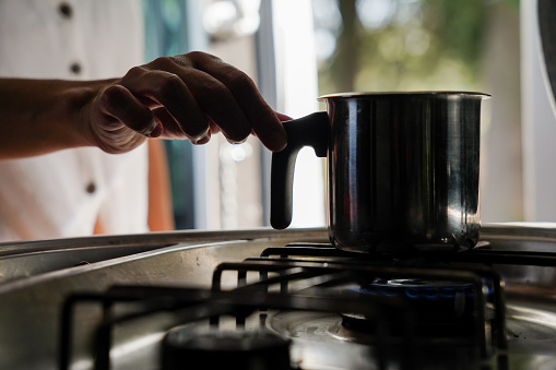 Female hand putting a kettle on the gas stove with hot drink in a van