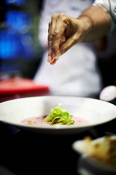 Chef preparing cold summer soup with sliced zucchini pieces on it.