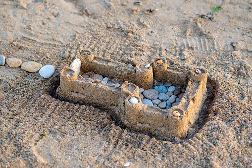 Children's sand castle on beach. Summer vacation. Sea stones and shells in sand