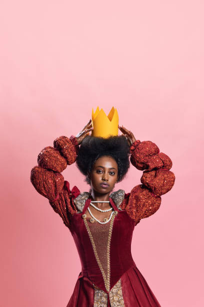 królewska elegancja. portret młodej, pięknej afrykańskiej kobiety, średniowiecznej księżniczki w zabytkowej sukni z papierową koroną na różowym tle studyjnym - women crown princess 20s zdjęcia i obrazy z banku zdjęć