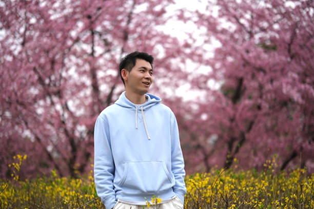istock cute asian young man with pink sakura trees bokeh 1700506663