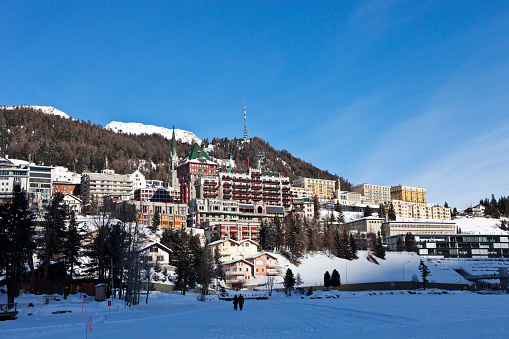 As the sun rises more and more of the city of St. Moritz in the Engadine alps in Switzerland is bathed in sunlight. The photograph was taken on a freezing cold winter morning from the ice covered lake of St. Moritz.