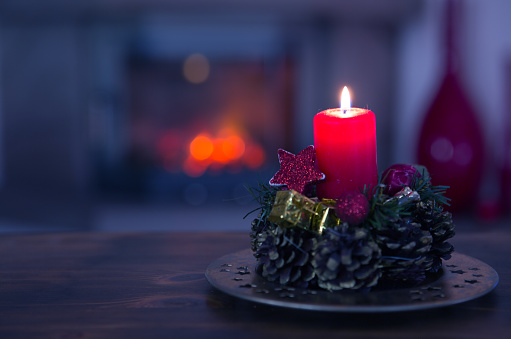 Glowing Advent candle and fireplace in blurred background