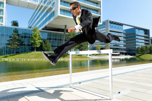 cool guy in business suit running over hurdle on office campus outdoors in summer
