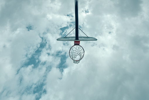 Basketball hoop high in the sky during the daytime with clouds in background.